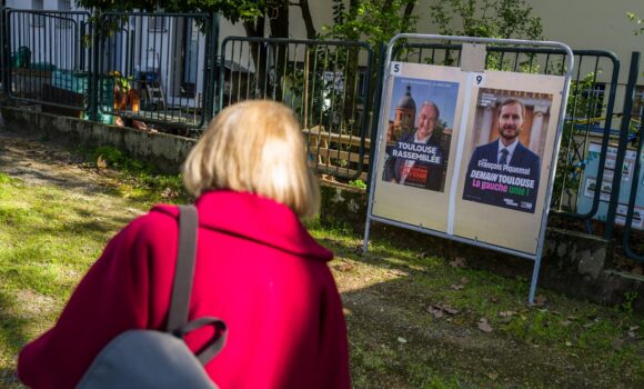 Toulouse, 20 mars 2026. Une personne regarde les panneaux électoraux en vue du second tour des élections municipales le 22 mars 2026 avec l’actuel Maire de Toulouse Jean Luc Moudenc (G) et Francois Piquemal pour LFI (D). Photo : Frédéric Scheiber / Hans Lucas via AFP