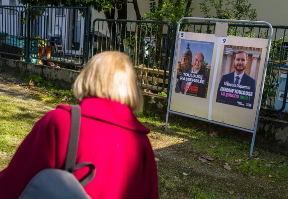 Toulouse, 20 mars 2026. Une personne regarde les panneaux électoraux en vue du second tour des élections municipales le 22 mars 2026 avec l’actuel Maire de Toulouse Jean Luc Moudenc (G) et Francois Piquemal pour LFI (D). Photo : Frédéric Scheiber / Hans Lucas via AFP